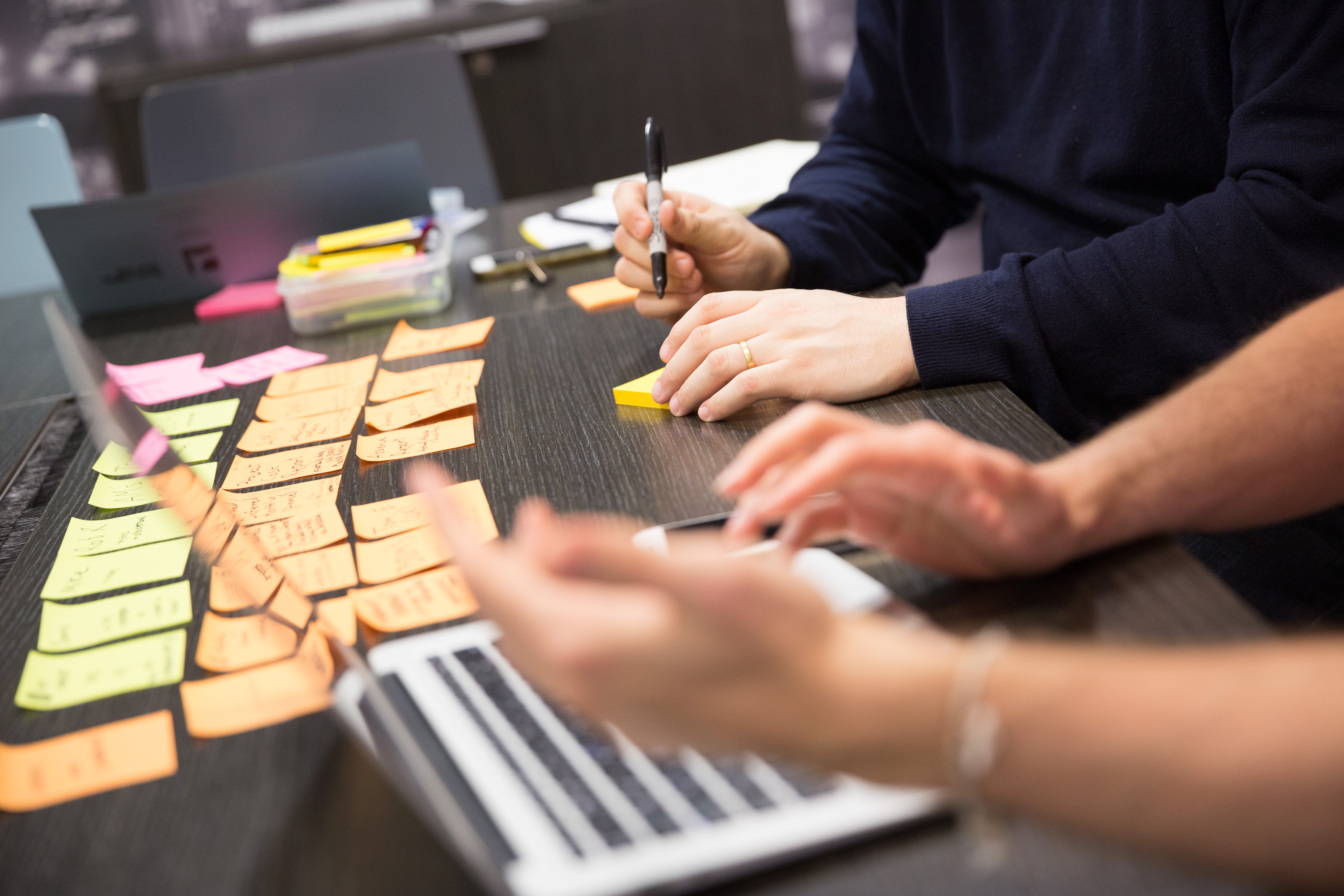 Two people writing on post-it notes with a laptop in the foreground