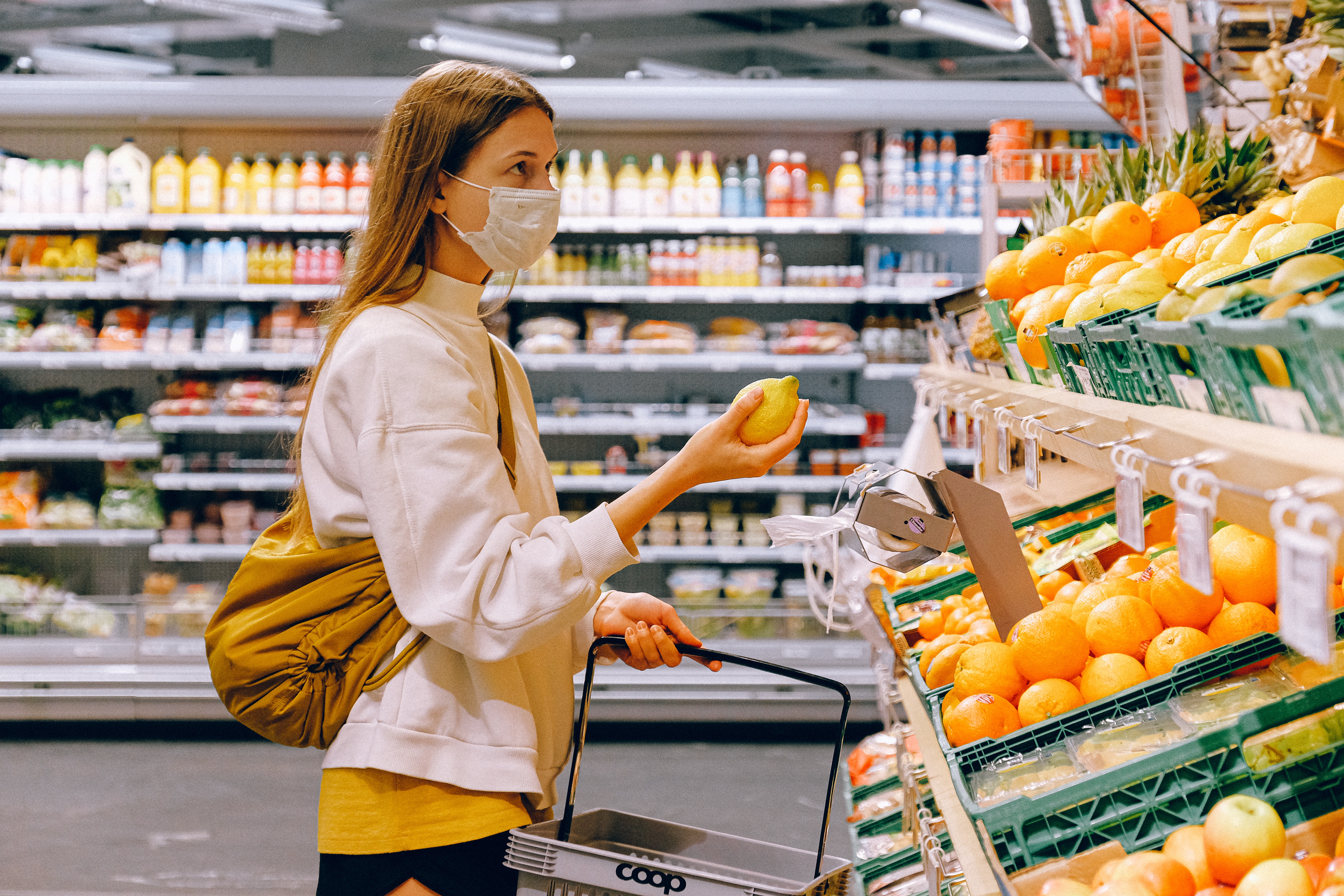 Woman wearing a face mask in a supermarket, looking at a display of fruit