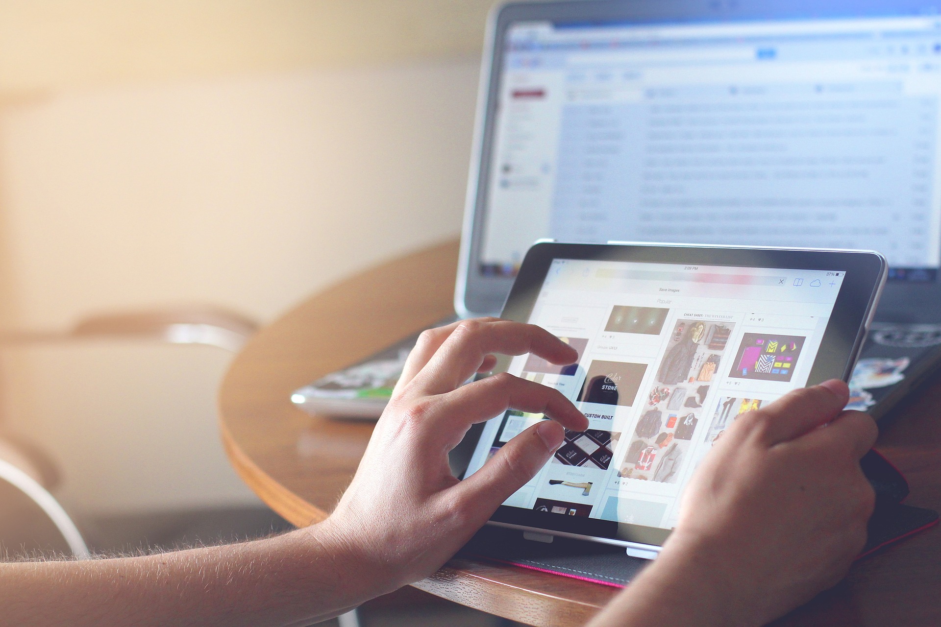 Person using a tablet device with a laptop in the background