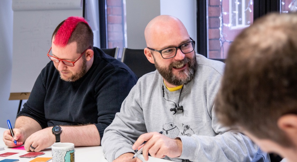 Two men having a discussion at a table, one with a laptop