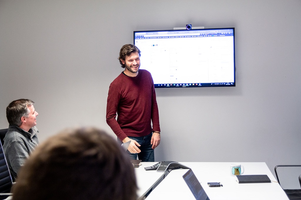 Man stood in front of screen delivering a presentation to people sat watching