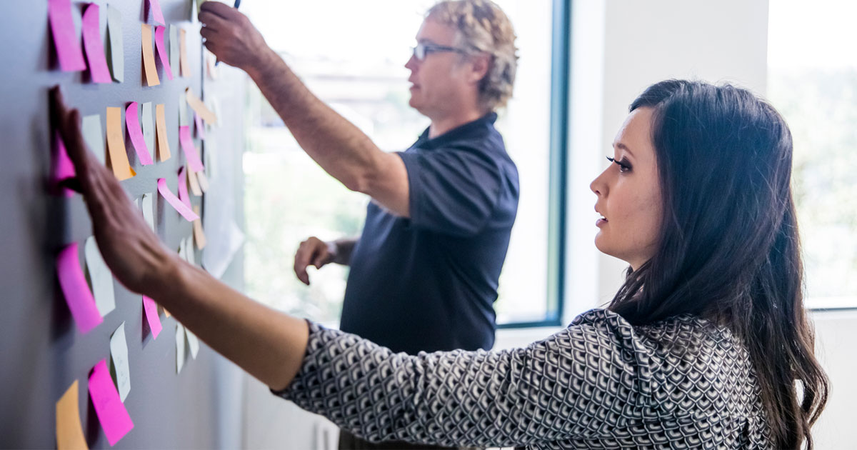 Two people adding post-it notes to a wall