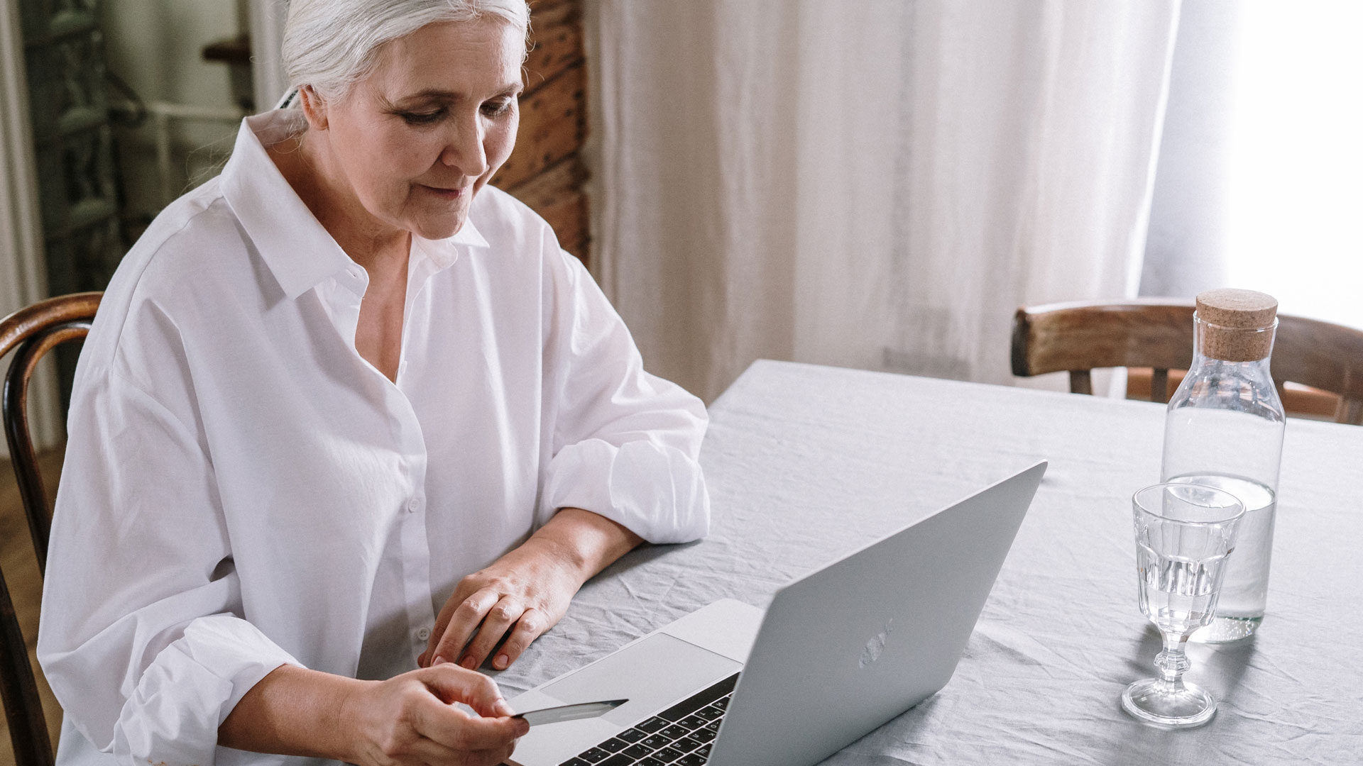 Woman holding credit card in front of laptop, with water jug and glass