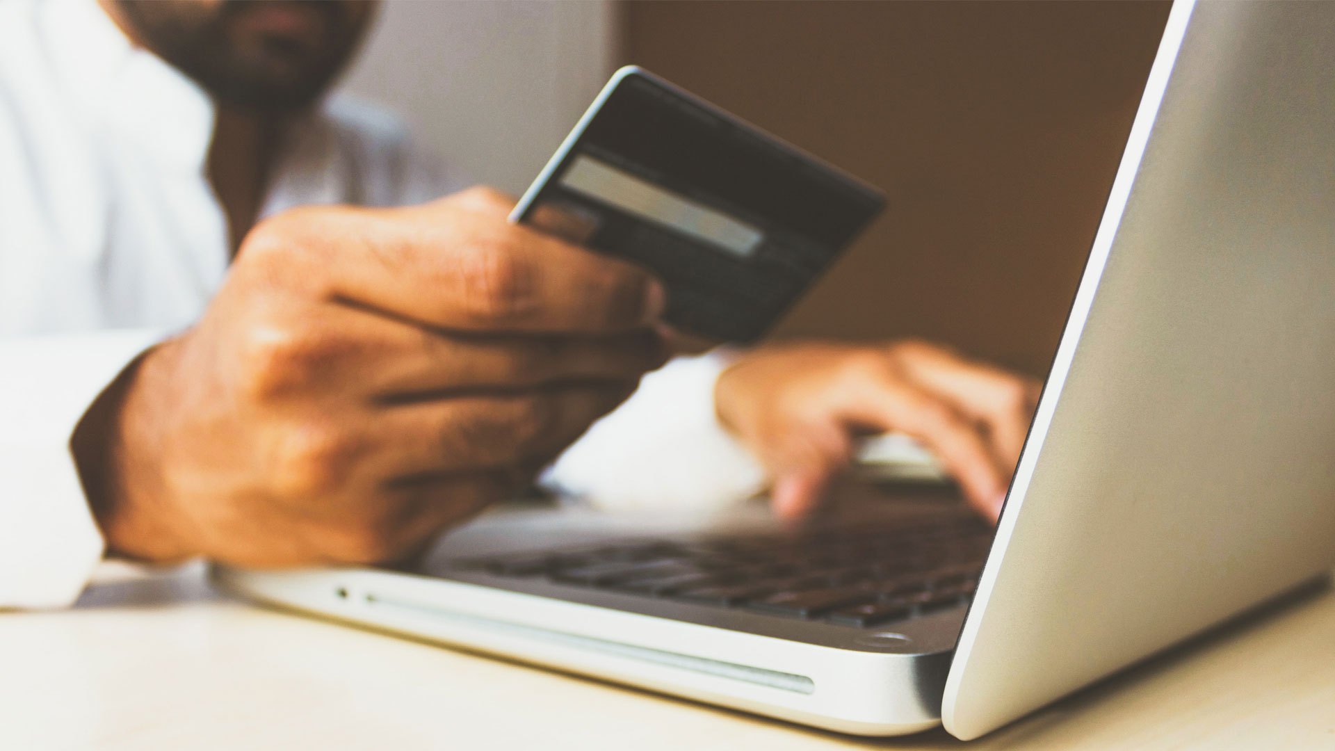 Close up of person holding credit card and using laptop