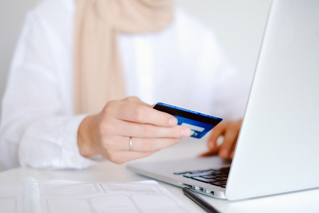 Close up of person holding credit card and using laptop