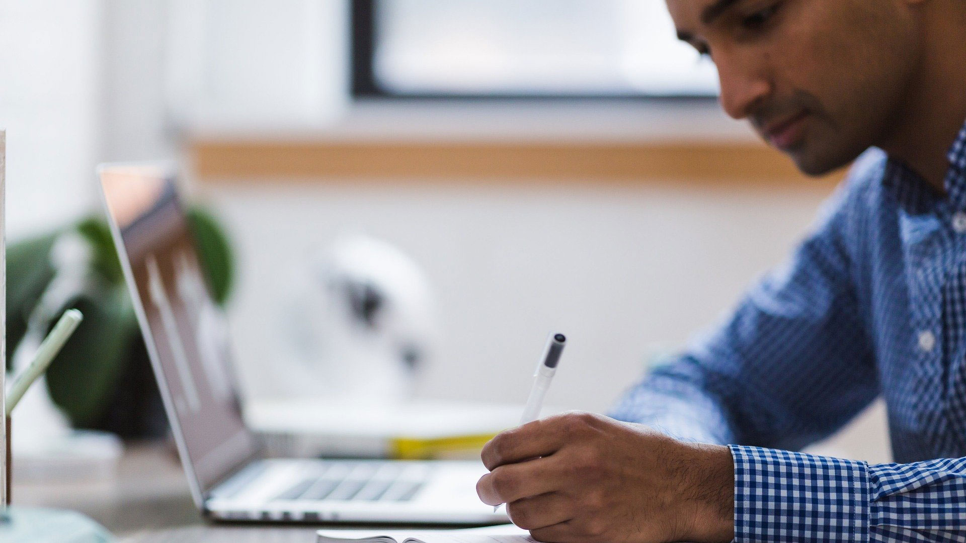 Person writing in a notebook with laptop in background