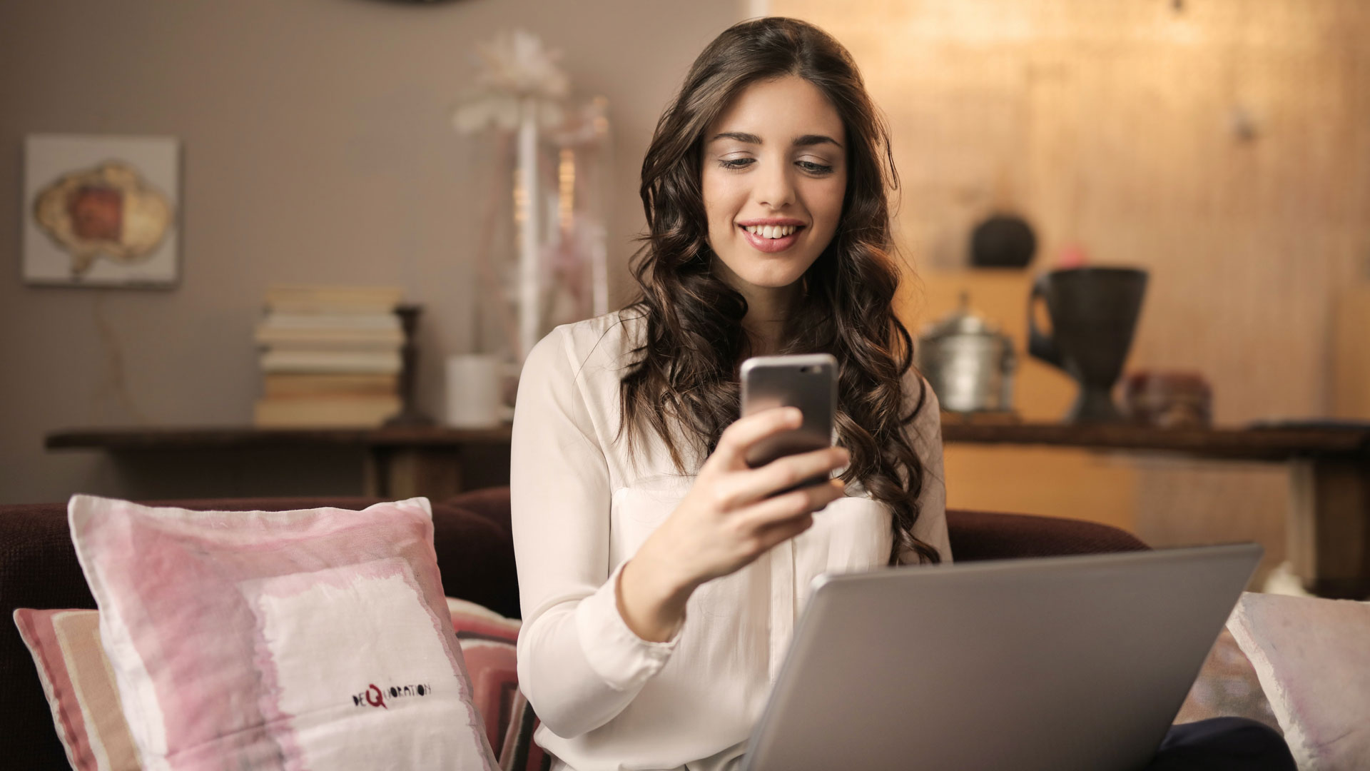 Woman sat on sofa with smartphone and laptop open