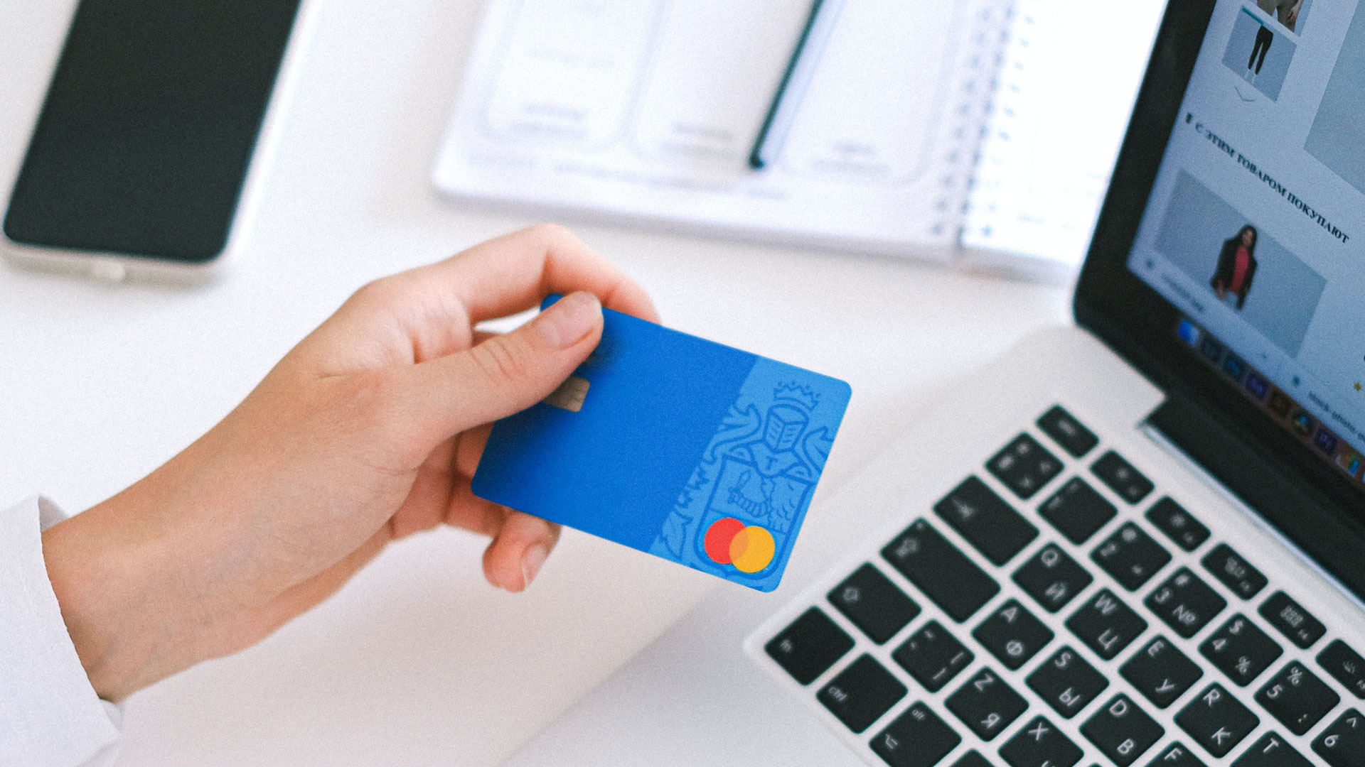 Person's hand holding a credit card, in front of laptop