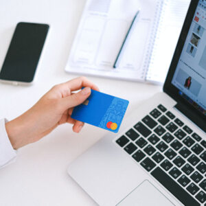 Person's hand holding a credit card, in front of laptop