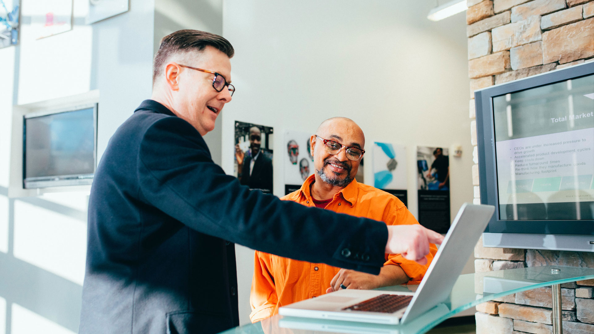 Two people having a discussion around a laptop, with one man pointing at the screen