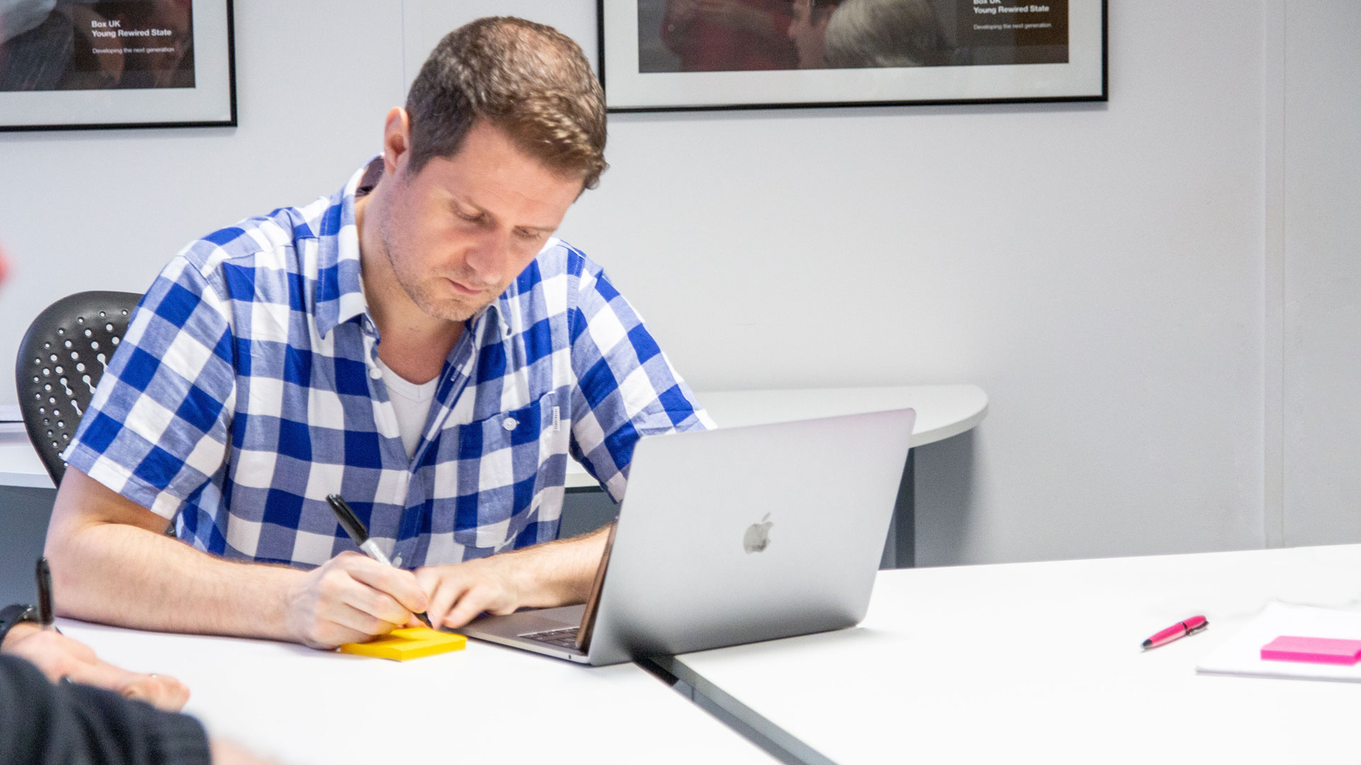 Person writing on a post-it note in front of a laptop