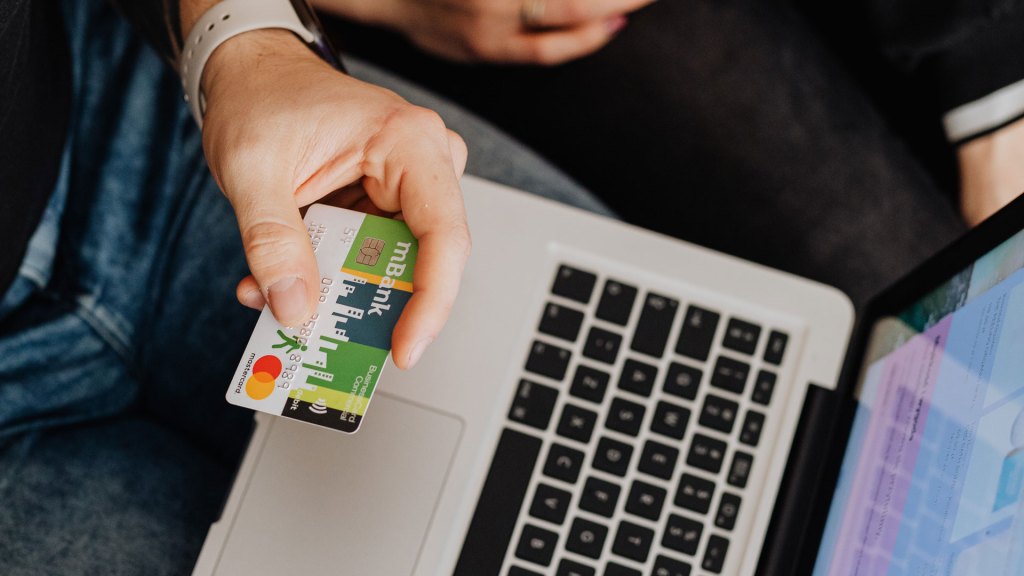 Person holding payment card with laptop in background