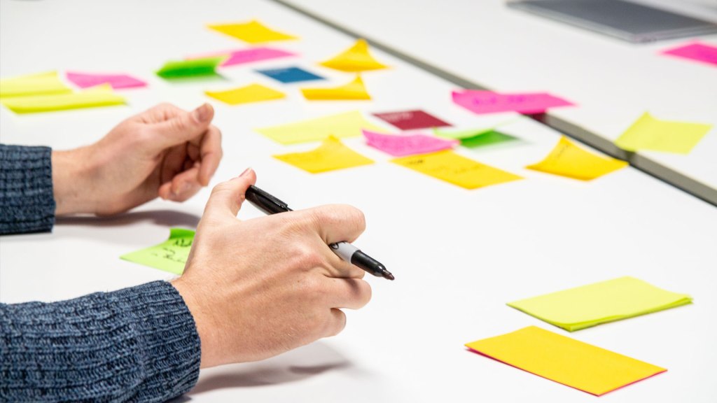 Person writing on a post-it note with multiple notes in background