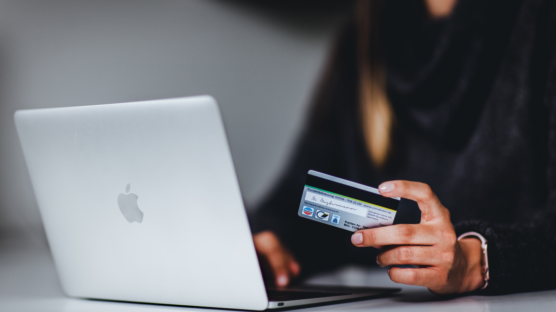 Close up of person holding payment card and using laptop