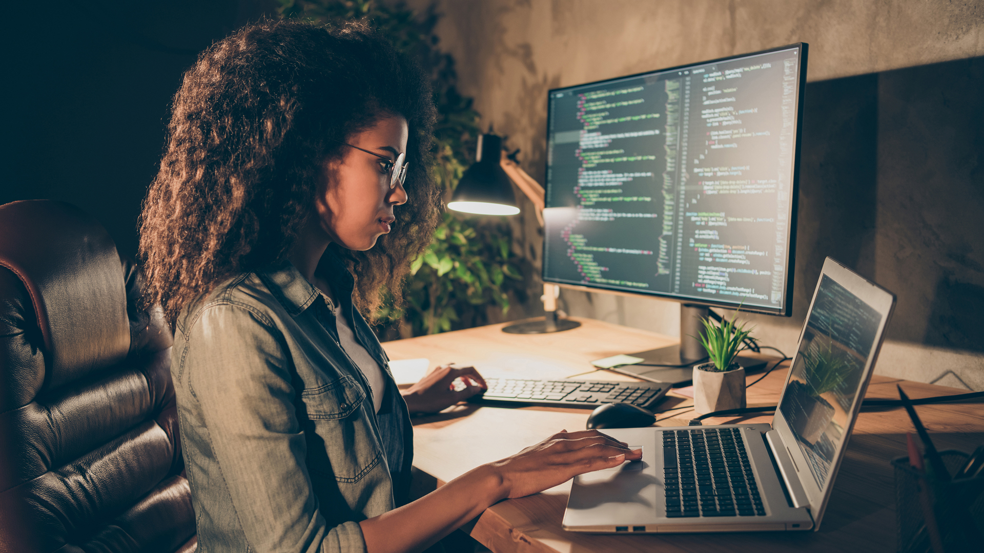 Person using laptop with larger monitor in background