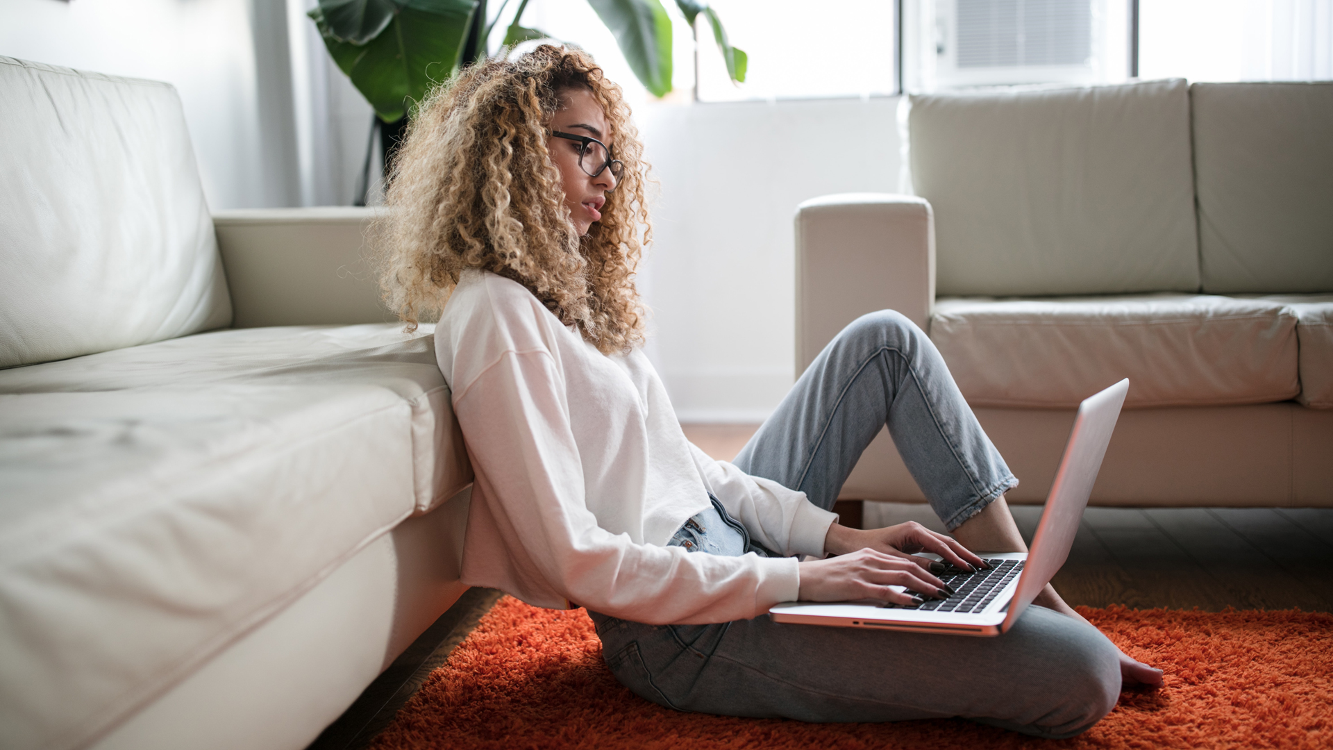 Person sat on the floor with a laptop, and sofas in the background